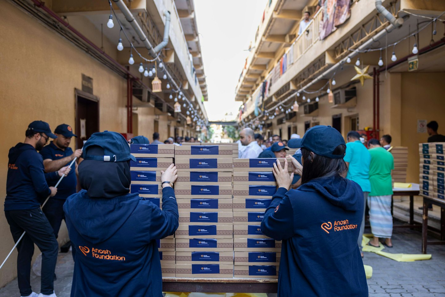 Volunteers stack and distribute cardboard boxes outdoors between buildings.