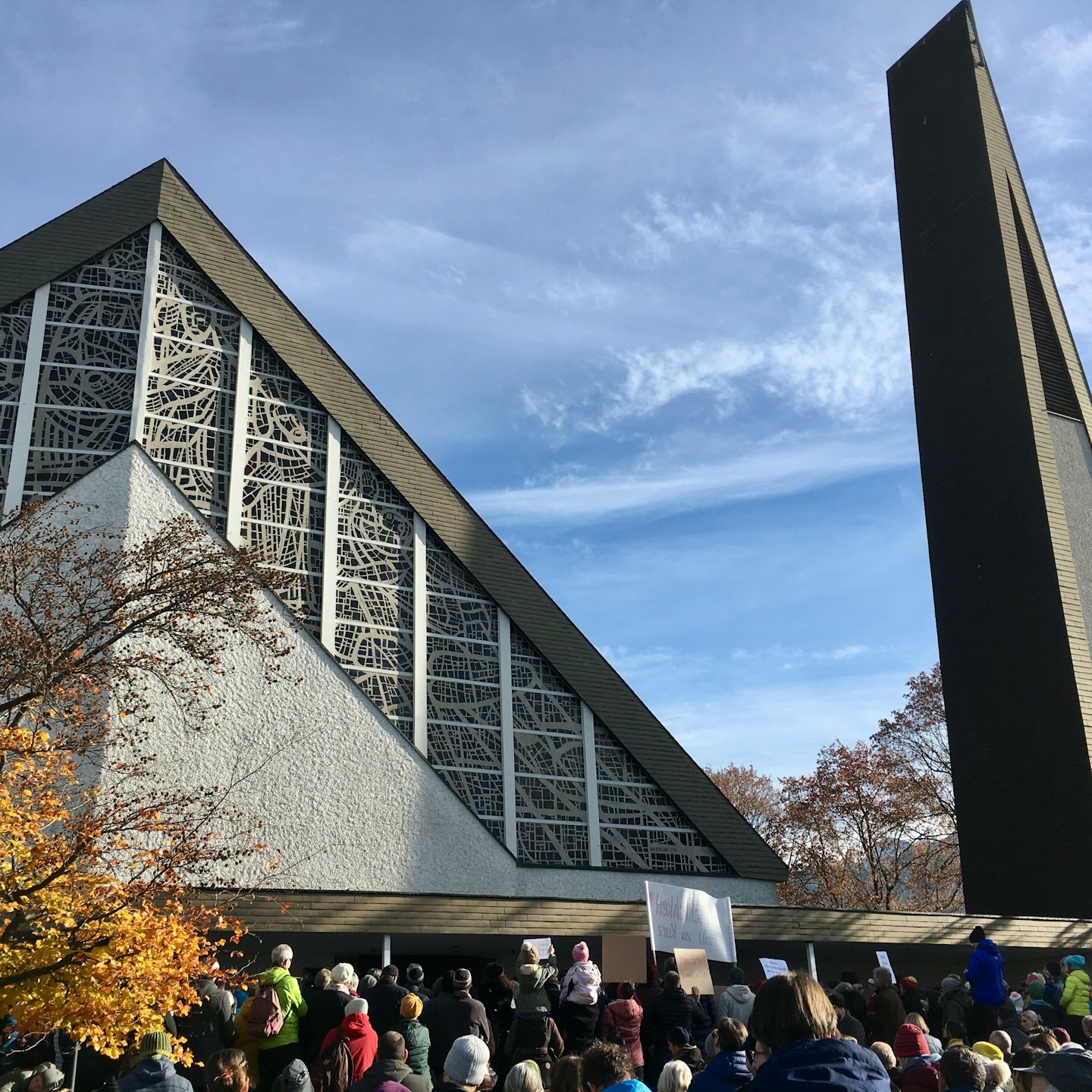 A crowd holding protest signs gathers before a modern church.
