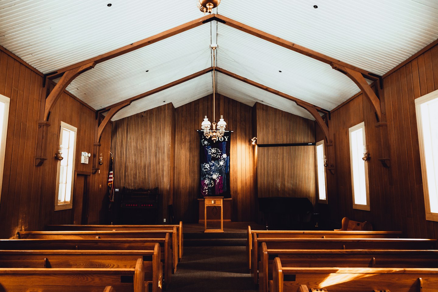 Wooden pews line the aisle of a rustic wooden church.