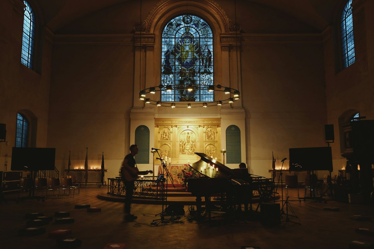 Musicians performing with guitar and piano in a candlelit church.